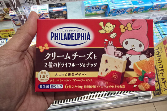 Beppu, Japan: Jan 07, 2026: A hand holds a box of Philadelphia cream cheese dessert featuring My Melody character branding, containing cranberry, orange peel, and almond pieces, at YouMe Food Market.