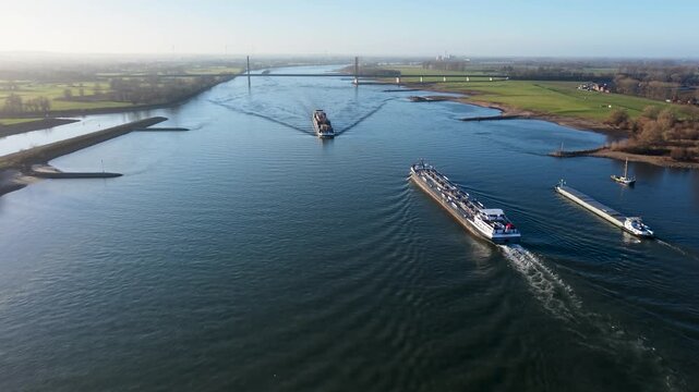 Aerial drone view of a long industrial tanker barge cruising past the historic town of Rees on the Rhine River, Germany. Picturesque riverside architecture and city skyline.