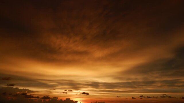A sunrise sky timelapse video footage featuring rippled altocumulus clouds and layered stratus glowing in warm golden hues, gradually revealing soft morning light across a calm horizon.
