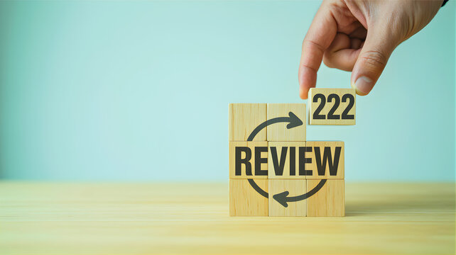Hand placing the number 222 on wooden blocks forming the word REVIEW, symbolizing continuous improvement and evaluation