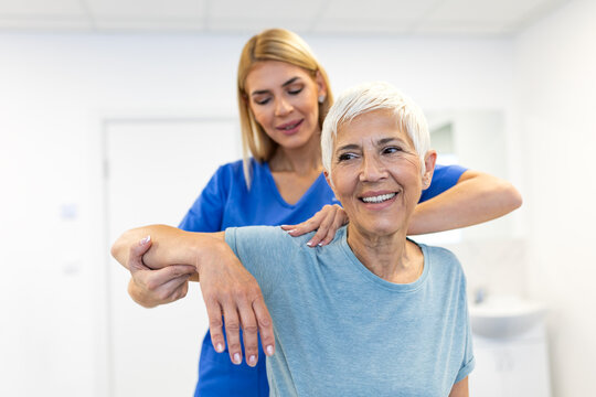 Physiotherapist helping senior woman with shoulder rehabilitation exercises. Manual therapy for joint mobility in a medical clinic. Healthcare and medicine concept. Specialist treating elderly patient