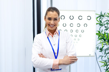Portrait of a happy female optometrist smiling in a clinic. Professional eye doctor standing in...
