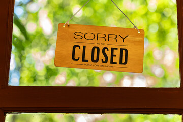Close up of a “Sorry we are closed” sign hanging on a door with blurred green background....