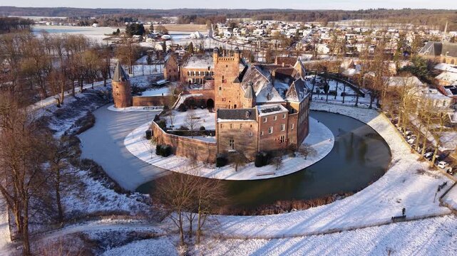 Aerial winter view of Huis Bergh Castle in s-Heerenberg, Netherlands. Majestic medieval fortress with brick towers surrounded by a frozen moat and snow-covered landscape under bright sunlight.