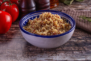 Healthy cooked tri-color quinoa in a bowl with fresh tomatoes and rosemary on a rustic wooden table