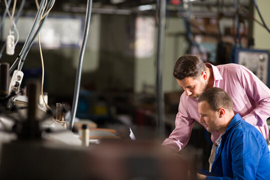 Professional supervisor and industrial worker discussing production process on a factory floor, teamwork in manufacturing plant.