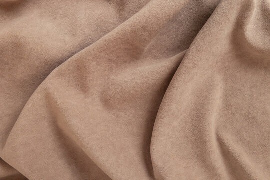 High-quality close-up of soft brown velour or faux suede fabric. The matte surface features gentle, flowing draping folds and soft shadows, creating a luxurious and tactile texture.