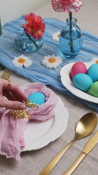 Easter table setting with dyed eggs, pink chiffon napkin and gold cutlery on linen and a blue runner, styled with flowers and bright copy space for seasonal design