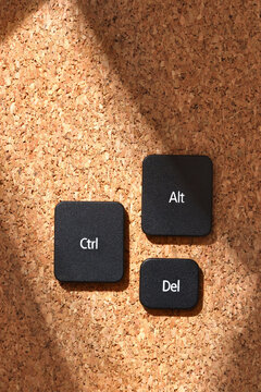Black keyboard keys "Ctrl", "Alt", "Del" on a cork bulletin board in soft sunlight, symbolizing the classic computer reboot shortcut. Top view.