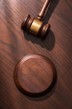 Close-up of a judge&rsquo;s gavel with sound block against a polished dark brown wood background in soft sunlight, symbolizing justice and legal authority in a courtroom setting. Copy space.