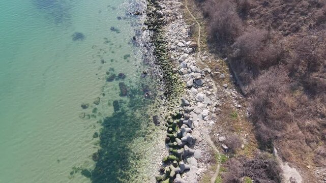 Aerial drone view of rocky coastline meeting clear turquoise water with underwater patterns visible