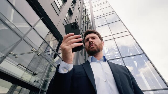 Confused mature Caucasian business man with mobile phone lost signal city office building male businessman searching WiFi connection problem online chatting app trouble smartphone issue street outdoor