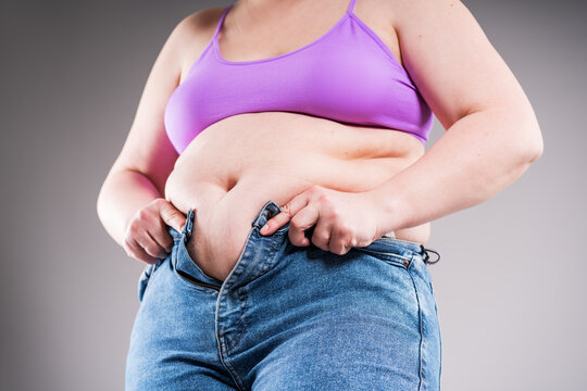 Overweight woman struggling to button too tight jeans over her belly, concept of weight gain and need for dieting