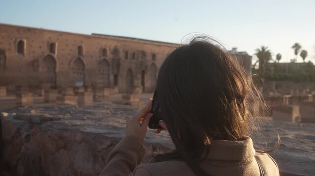 Young tourist woman recording sunset over Koutoubia Mosque gardens with smartphone