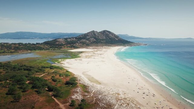 Aerial orbit left around Praia de Louro in Galicia, Spain revealing turquoise shoreline and Monte Louro mountain backdrop.