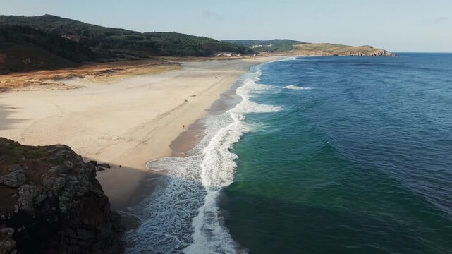 Drone descending from coastal cliffs toward Atlantic waves along the remote shoreline of Praia do Rostro in Galicia.