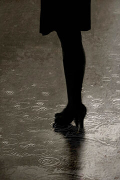 Woman's legs in high heels reflecting on wet city street in rain