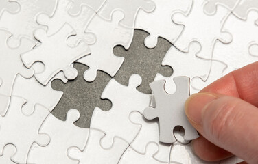 Fototapeta premium Puzzle pieces being arranged with one piece being placed in an empty spot on a grey surface