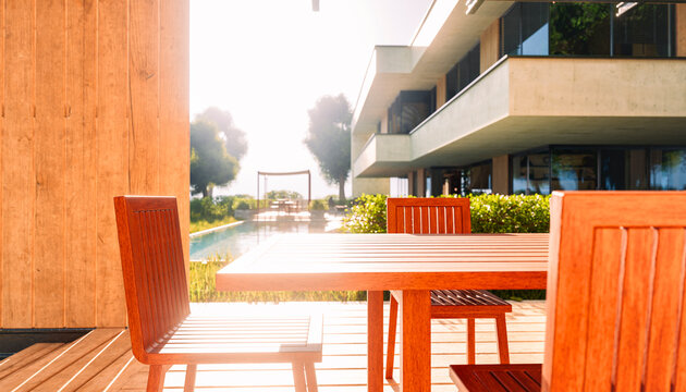 Modern house with wooden patio furniture by outdoor pool in summer