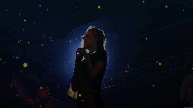 Backlit framing female singer hairflip and singing for gig crowd golden particles rising around her