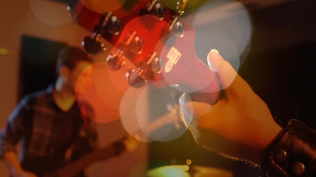 Guitarist adjusting red neck tuning pegs, causing strings vibrating with bokeh overlaying practice