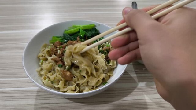 Noodles sit in a bowl with meat and greens
