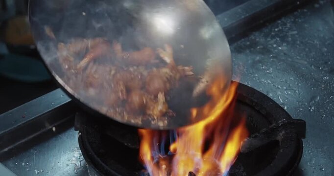 Chef stir frying battered shrimp in a hot wok over a gas flame