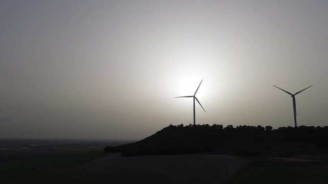 Drone lateral tracking shot of wind turbines at sunset in hazy sky &ndash; renewable energy aerial footage