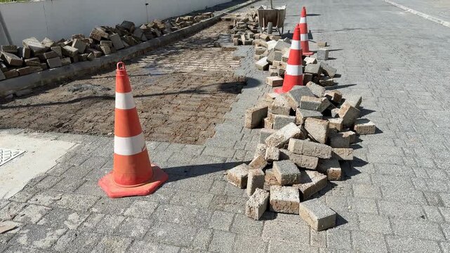 Road construction scene with orange traffic cones and scattered paving stones in a sunny setting