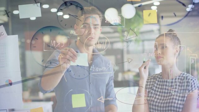 Two coworkers testing sticky note placement and drawing diagrams on glass during business planning