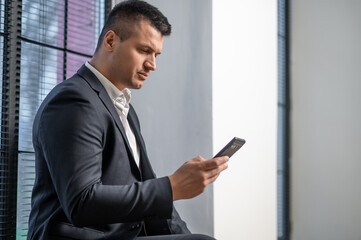 Fototapeta premium Male focused on smartphone while posing in modern workplace