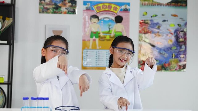 Two Young Asian Girls in Lab Coats Pointing Down in Science Class