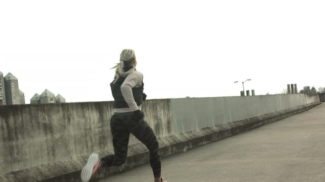 A medium shot captures a person jogging along an urban bridge, their back to the camera. The runner, likely in 20s, wears athletic attire suitable for sport training.