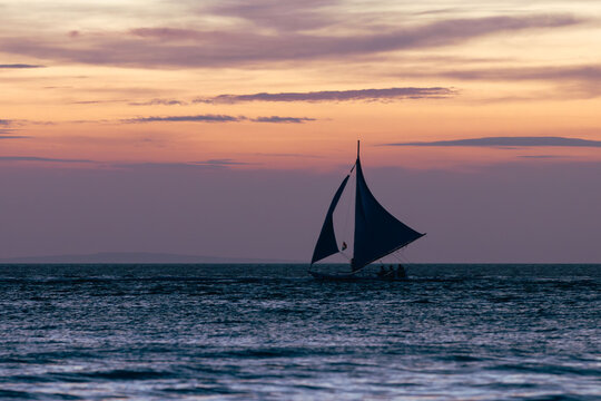 View of a sailboat gliding across the serene waters, silhouetted against the vibrant hues of the setting sun, casting a peaceful glow on the horizon, Malay, Western Visayas, Philippines.