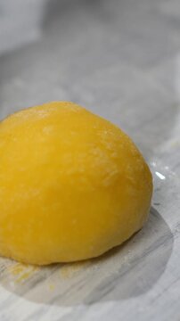 Vertical video. Baker hands shape form and add powdered sugar to mango mochi cake in bakery closeup. Professional confectioner decorates Japanese dessert with tropical fruits in kitchen. Healthy sweet
