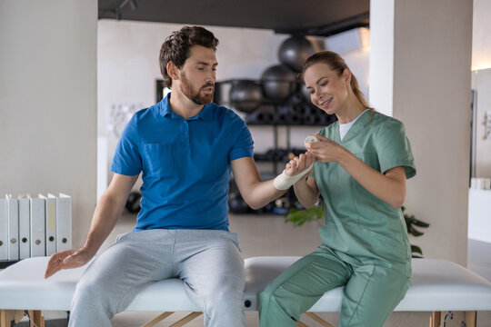 Female therapist applying elastic bandage to man hand