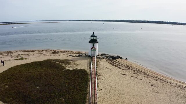 Aerial fly-in toward Brant Point Lighthouse in Nantucket, Massachusetts, revealing the sandy shoreline and calm harbor waters from a cinematic drone perspective.