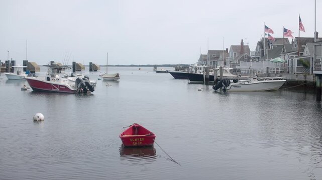 Handheld shot of a red &ldquo;Sunken Ship&rdquo; dinghy floating in calm Nantucket Harbor, framed by docked boats and waterfront homes in soft coastal light.