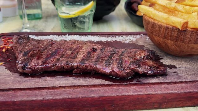Skirt steak with French fries, coarse salt and pepper on a wooden board served in an Argentine restaurant. High quality 4k footage