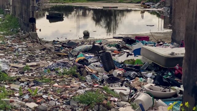 Large pile of illegal dumping and overflowing trash near a flooded riverbank, highlighting environmental pollution and neglect