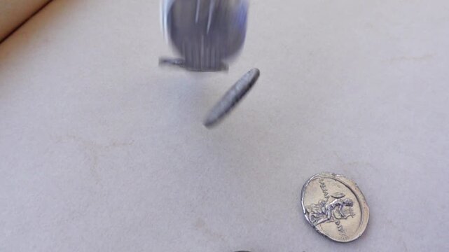 Ancient Roman silver coins falling on a neutral background.