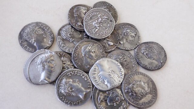 Ancient Roman silver coins falling on a neutral background.