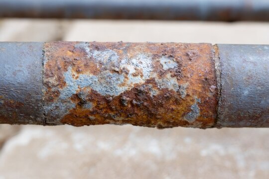 Detailed macro shot of a corroded steel pipe. The rough, rusty texture of weathered metal shows significant decay and oxidation