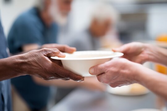 Volunteer serving a warm meal to a senior person at a soup kitchen. Close-up on hands showing charity, donation, and community support