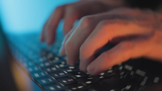 Typing on a laptop keyboard Coding or hacking in blue and orange lighting, suitable for concepts such as cybersecurity, coding, online work, data entry, digital communication, and technology at night.