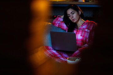 Woman wearing comfortable pajamas, feeling tired while watching content or working on a notebook...