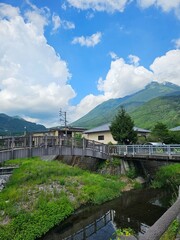Fototapeta premium Scenic View of a Wooden Bridge and Stream in Yufuin Village with Mt. Yufu, Japan