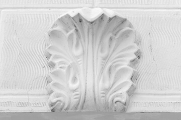 White ornamental plaster acanthus leaf relief mounted on a textured wall, showcasing classical architectural molding and decorative detail. High-contrast monochrome image emphasizing texture, symmetry © evannovostro
