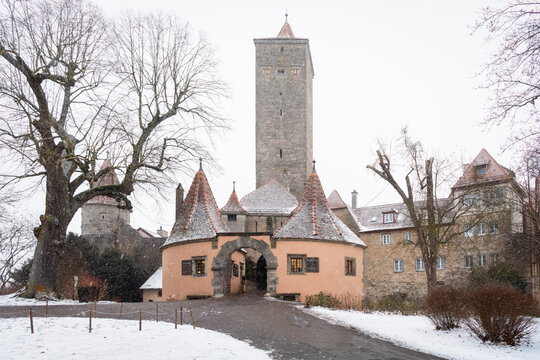 View of a medieval gate and tower stand tall amidst a dusting of winter snow, a scene of historical charm and quiet beauty, Rothenburg ob der Tauber, Bavaria, Germany.