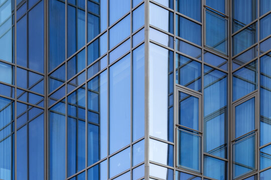 Modern blue glass facade of an office building with reflective windows, intersecting metal frames and geometric patterns conveying urban architecture, minimalism, transparency and contemporary design.